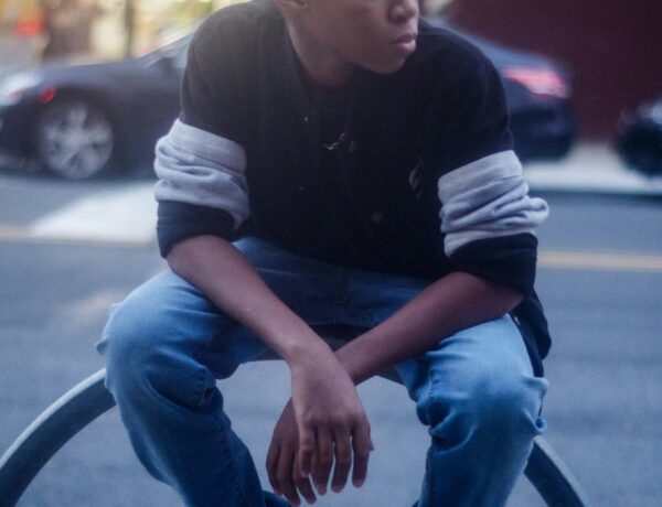 A teenager in casual wear sits on a street railing, showcasing urban style.